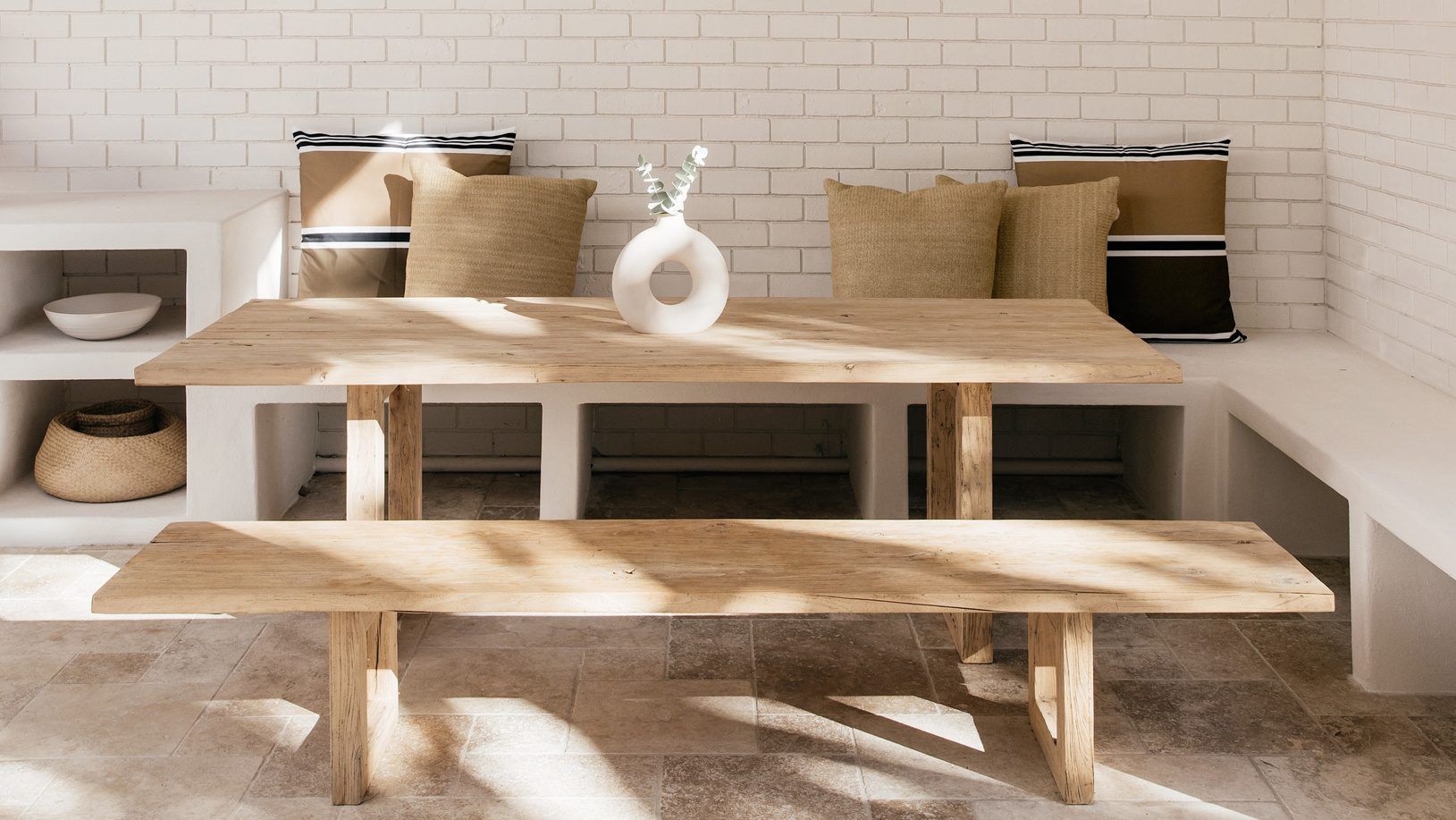 A timber dining table and bench in a light, well-kept room
